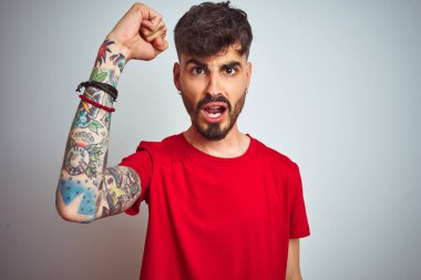 Kırmızı tişörtlü genç adam izole edilmiş beyaz arka planda öfkeli ve kızgın duruyor öfkeyle bağırırken yumruğunu kaldırıyor. Öfke ve agresif kavram.