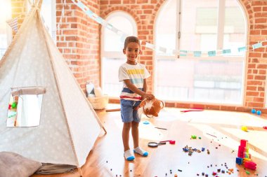 Güzel Afrikalı Amerikalı çocuk anaokulunda bir sürü oyuncakla at oyuncağıyla oynuyor.