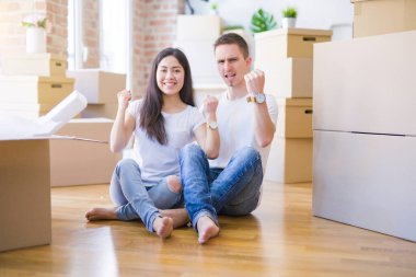 Genç ve güzel bir çift, yeni evlerinde karton kutuların etrafında oturmuş gururla bağırıyor ve zaferi ve başarıyı kutluyor.