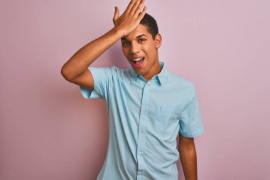 Soyutlanmış pembe arka plan üzerinde duran mavi tişörtlü genç, yakışıklı Arap adam hata sonucu el ele tutuşarak şaşırdı, unutma. Unuttum, kötü hafıza konsepti.