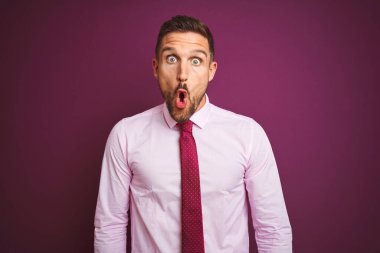 Zarif gömlek ve kravat takan genç bir iş adamı. Mor izole edilmiş arka planda korkmuş ve şok olmuş bir halde..