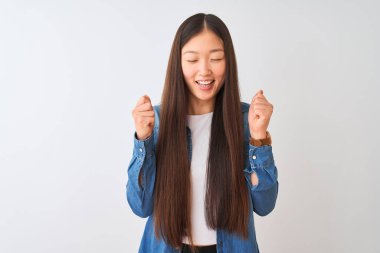 İzole edilmiş beyaz arka plan üzerinde duran genç Çinli kadın. Başarının heyecanı içinde kollarını kaldırmış ve gözleri kapalı zaferi kutluyor. Kazanan konsept.