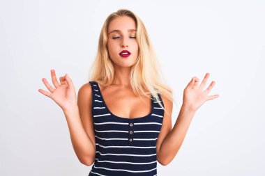 İzole edilmiş beyaz arka plan üzerinde duran sıradan çizgili tişört giyen genç ve güzel bir kadın rahatla ve gözleri kapalı meditasyon yaparken parmaklarınla gülümse. Yoga konsepti.