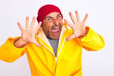 Yağmurluk ve yün şapka giyen orta yaşlı bir adam izole edilmiş beyaz arka plan üzerinde duruyor ve parmaklarını on numarayı gösterirken kendinden emin ve mutlu bir şekilde gülümsüyor..