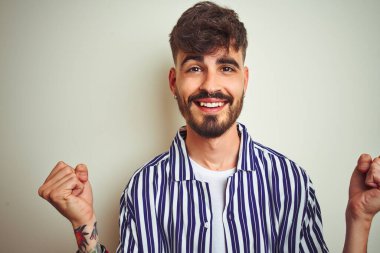 İzole edilmiş beyaz arka plan üzerinde duran çizgili tişörtlü genç adam kollarını kaldırarak ve açık gözlerle başarıyı kutluyor ve şaşırıyor. Kazanan konsept.