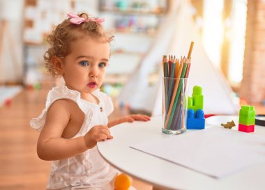 Renkli oyun odasında beyaz güzel bir bebek oyuncaklarla oynuyor. Anaokulunda renkli kalemlerle mutlu ve eğlenceli çizimler..