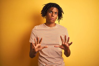 Sarı arka plan üzerinde duran çizgili tişörtlü Afro bir adam. Avuçlarını kaldırıyor, reddediyor ve iğrenç bir ifadeyle reddediyor. Dur ve yasakla.