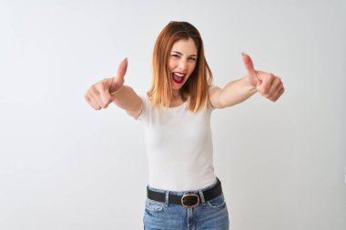 Güzel kızıl saçlı kadın el ile olumlu jest yapıyor onaylayan izole beyaz arka plan üzerinde duran rahat t-shirt giyen, başparmak kadar gülümseyerek ve başarı için mutlu. Kazanan jest.