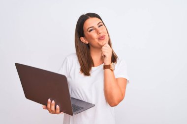 Bilgisayarla çalışan güzel genç bir kadın beyaz arka plan üzerinden kameraya bakarak kollarını kavuşturup, ellerini çenesine kaldırarak gülümsüyor. Olumlu düşünüyorum..