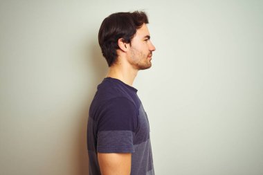 Dövmeli genç yakışıklı bir adam, izole edilmiş beyaz bir arka plan üzerine günlük tişört giyiyor, rahat bir görünüm takınıyor, kendine güvenen bir gülümsemeyle doğal bir yüz ifadesi sergiliyor..