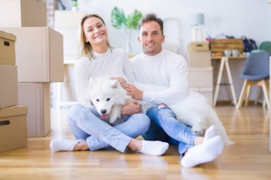Karton kutular etrafında yeni evde yerde oturan köpek ile genç güzel çift