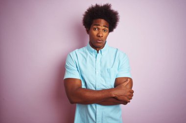 Afro saçlı, mavi tişörtlü genç bir Amerikalı. İzole edilmiş pembe arka plan üzerinde duruyor. Kuşkucu ve gergin. Negatif kişi.