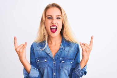 İzole edilmiş beyaz arka plan üzerinde dikilen sıradan bir kot giyen genç ve güzel bir kadın çılgın bir ifadeyle elleri havada rock sembolü yapıyor. Müzik yıldızı. Ağır müzik konsepti.