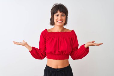 Kırmızı yaz tişörtü giyen genç ve güzel bir kadın izole edilmiş beyaz arka planda durup gülümseyerek avuçlarını açıyor, sunuyor ve reklam karşılaştırması yapıyor ve dengeyi sağlıyor.