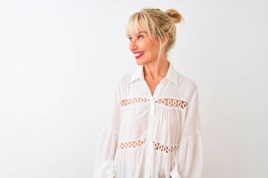 Orta yaşlı kadın, izole edilmiş beyaz arka planda dikilip yüzünde gülümseme, doğal bir ifade ile yan yana duran sıradan bir gömlek giyiyor. Kendinden emin gülen.