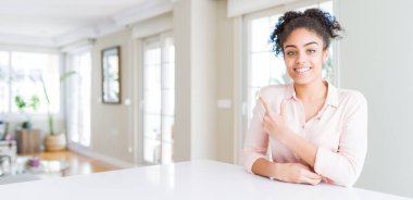 Afro saçlı, neşeli, yüzünde gülümsemesi olan, mutlu ve doğal bir ifadeyle elini ve parmağını yana doğru gösteren güzel Afro-Amerikan kadınının geniş açısı.