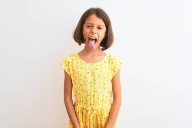 Sarı çiçekli elbise giyen güzel bir kız çocuğu izole edilmiş beyaz arka planda dikiliyor ve komik bir ifadeyle dilini dışarı çıkarıyor. Duygu kavramı.