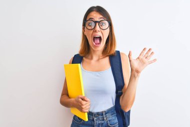 Sırt çantası ve kitap takan güzel kızıl saçlı bayan çok mutlu ve heyecanlı, kazanan yüz ifadesi zaferi büyük bir gülümsemeyle kutluyor ve ellerini kaldırıyor.