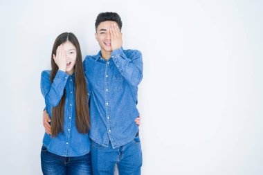 Güzel, genç Asyalı bir çift beyaz bir arka planda bir gözünü eliyle kapatıyor, yüzünde kendine güvenen bir gülümseme ve sürpriz bir duygu var..