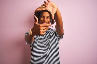 Siyah saçlı, donanma tişörtü ve şapkası olan, izole edilmiş pembe arka planda gülümseyen, elleri ve parmakları gülen yüzlü Afro-Amerikan bir adam. Yaratıcılık ve fotoğrafçılık kavramı.