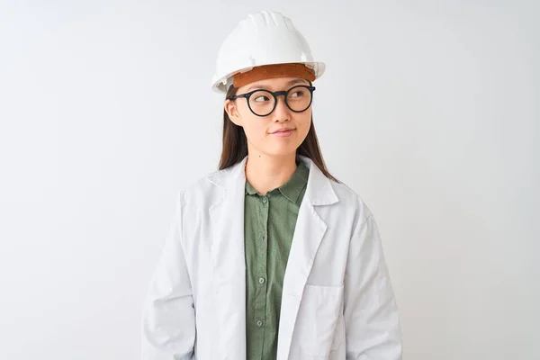 若いです中国のエンジニア女性身に着けていますコートヘルメット眼鏡上の隔離された白い背景笑顔見て側に離れて考え — ストック写真