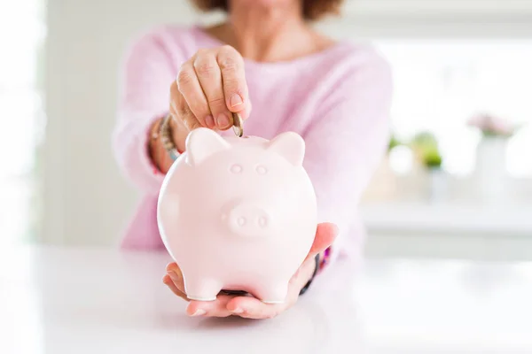 Close up de mulher sênior colocando uma moeda dentro do banco porquinho como sav — Fotografia de Stock