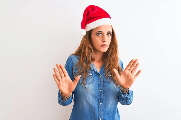 孤立した背景の上にクリスマスの帽子をかぶっている若い美しい赤毛の女性恐怖と嫌な表情で拒否と否定を示す手のひらを離れて移動します 止めて禁止 — ストック写真