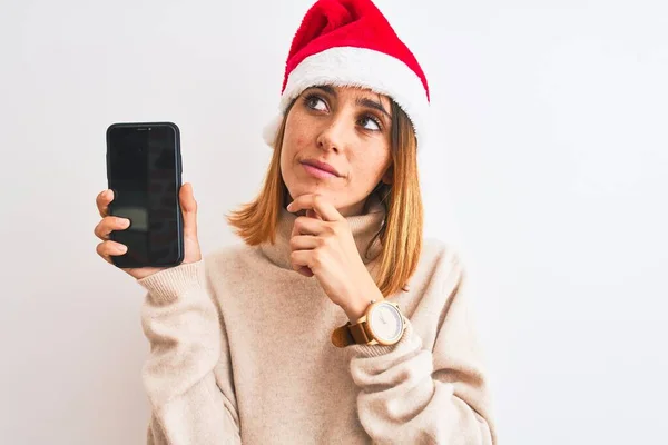 Beautiful Redhead Woman Wearing Christmas Hat Showing Smartphone Screen Serious — Stock Photo, Image