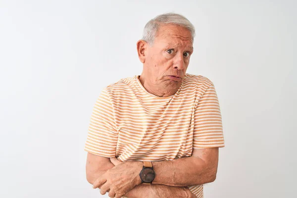 Senior grey-haired man wearing striped t-shirt standing over isolated white background shaking and freezing for winter cold with sad and shock expression on face