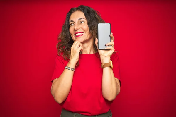 赤の隔離された背景深刻な顔の上にスマートフォンの画面を示す中年のシニア女性質問について考えて 非常に混乱したアイデア — ストック写真