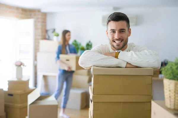 Young couple moving to a new home, handsome man smiling leaning on cardboard boxes