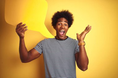 Genç Afrikalı Amerikalı bir adam konuşma baloncuğu tutuyor. Sarı arka planda duruyor. Çok mutlu ve heyecanlı.