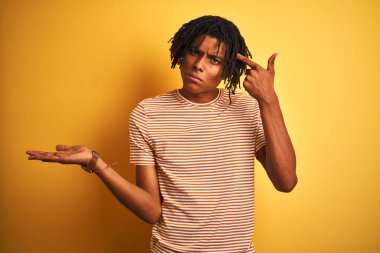 Rastalı tişörtlü Afro adam izole edilmiş sarı arka planda dikiliyor ve avuç içi açık bir şekilde fotokopi alanı gösterip alnını işaret etmekten rahatsız oluyor. Bunu bir düşün..