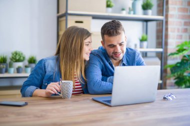 Genç çift bir kahve içme rahatlatıcı ve karton kutular etrafında bilgisayar laptop kullanarak, çok mutlu yeni bir eve hareket