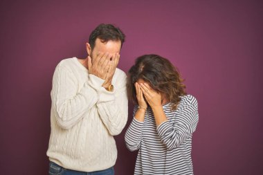 Güzel bir orta yaşlı çift, izole edilmiş mor arka plan üzerine kışlık süveter giyiyorlar ve ağlarken suratlarını ellerle kapatıyorlar. Depresyon kavramı.