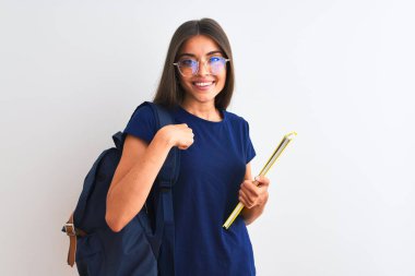 Sırt çantası gözlüklü genç bir bayan izole edilmiş beyaz arka plan üzerine kitap tutuyor ve kendini gösteren sürpriz bir yüz ifadesi var.