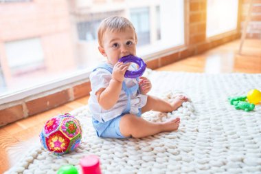 Anaokulunda battaniyenin üzerinde bir sürü oyuncağın etrafında oturan güzel çocuk.