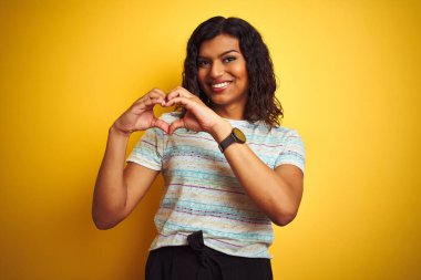 Güzel transseksüel kadın, izole edilmiş sarı arka planda tişört giyip, ellerinde kalp sembolü ve şekliyle gülümsüyor. Romantik konsept.