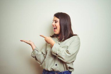 Izole arka plan üzerinde yeşil gömlek giyen genç güzel esmer kadın şaşırttı ve el ile sunarken kameraya gülümseyerek ve parmak ile işaret.