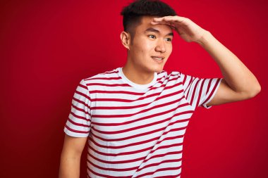 Asyalı genç bir Çinli çizgili tişört giyiyor. Kırmızı arka planda duruyor. Çok mutlu ve gülümsüyor. Konsept aranıyor.