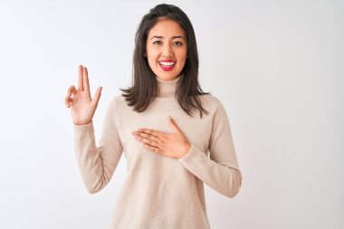 Balıkçı yaka kazak giyen güzel Çinli kadın izole edilmiş beyaz arka planda durup gülümsüyor ve el ve parmakları havada küfür ederek sadakat yemini ediyor.