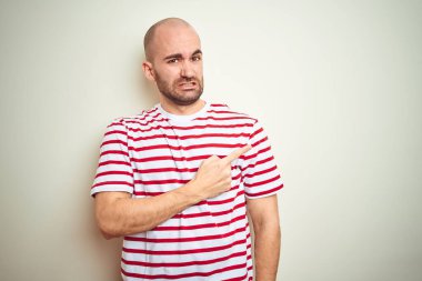 Sakallı, beyaz izole edilmiş arka plan üzerine normal çizgili kırmızı tişört giyen genç kel bir adam endişeli, endişeli ve şaşırmış bir ifadeye işaret ediyor.