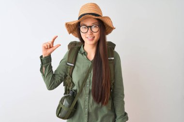 İzole edilmiş beyaz arka planda sırtüstü gözlük takan Çinli yürüyüşçü kadın gülümsüyor ve el hareketleriyle küçük beden işareti yapıyor ve kameraya bakıyor. Ölçü kavramı.