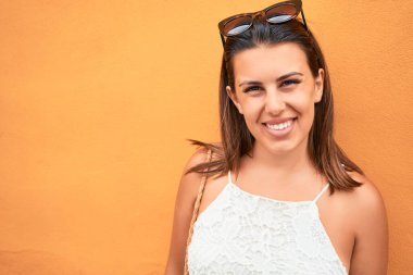 Turuncu duvara yaslanan güzel kız, güneşli bir yaz gününde gülümseyen genç arkadaş.