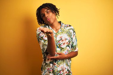 Tatilde saçı rastalı bir Afro adam izole edilmiş sarı arka planda tişört giyiyor kameraya bakıyor havada elle öpüşüyor ve çok güzel ve seksi. Aşk ifadesi.