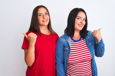 İzole edilmiş beyaz arka plan üzerinde dikilen, gülen yüzlü ve baş parmağıyla yüzünü gösteren genç ve güzel kadınlar..