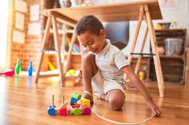 Güzel Afrikalı Amerikalı çocuk, anaokulundaki oyuncakların etrafında tahta bloklarla oyuncak eğitiyor.