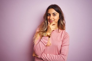 Pembe izole edilmiş arka planda kazak giyen genç ve güzel bir kadın kameraya kollarını kavuşturup gülümseyerek ve çenesini kaldırarak bakıyor. Olumlu düşünüyorum..