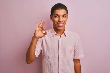 İzole edilmiş pembe arka planda duran rahat gömlekli genç, yakışıklı Arap adam el ve parmaklarıyla 