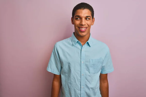 年轻英俊的阿拉伯男子穿着蓝色的衬衫 站在孤立的粉色背景上 微笑着看着旁边 目不转睛地想着 — 图库照片